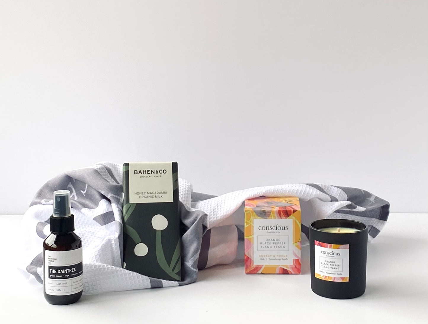 The Settle In Box contents - Conscious Candle Co aromatherapy candle, Richmond Candle Co room spray, Ladelle Bella Casa grey kitchen towels and Bahen & Co chocolate block - Gift Bento